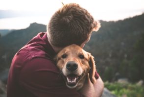 A man hugs a dog on top of a mountain